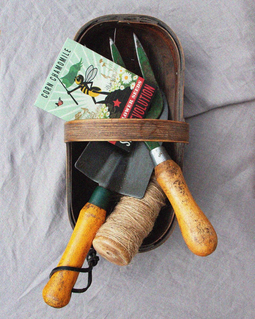 Set of gardening tools with a corn chamomile wildflower seeds packet on a soft grey background. Showcasing Seed Revolution's Corn Chamomile, Anthemis arvensis, chamomile, camomiles, british wild flower seeds, british wildflower seeds, uk wildflower seeds.