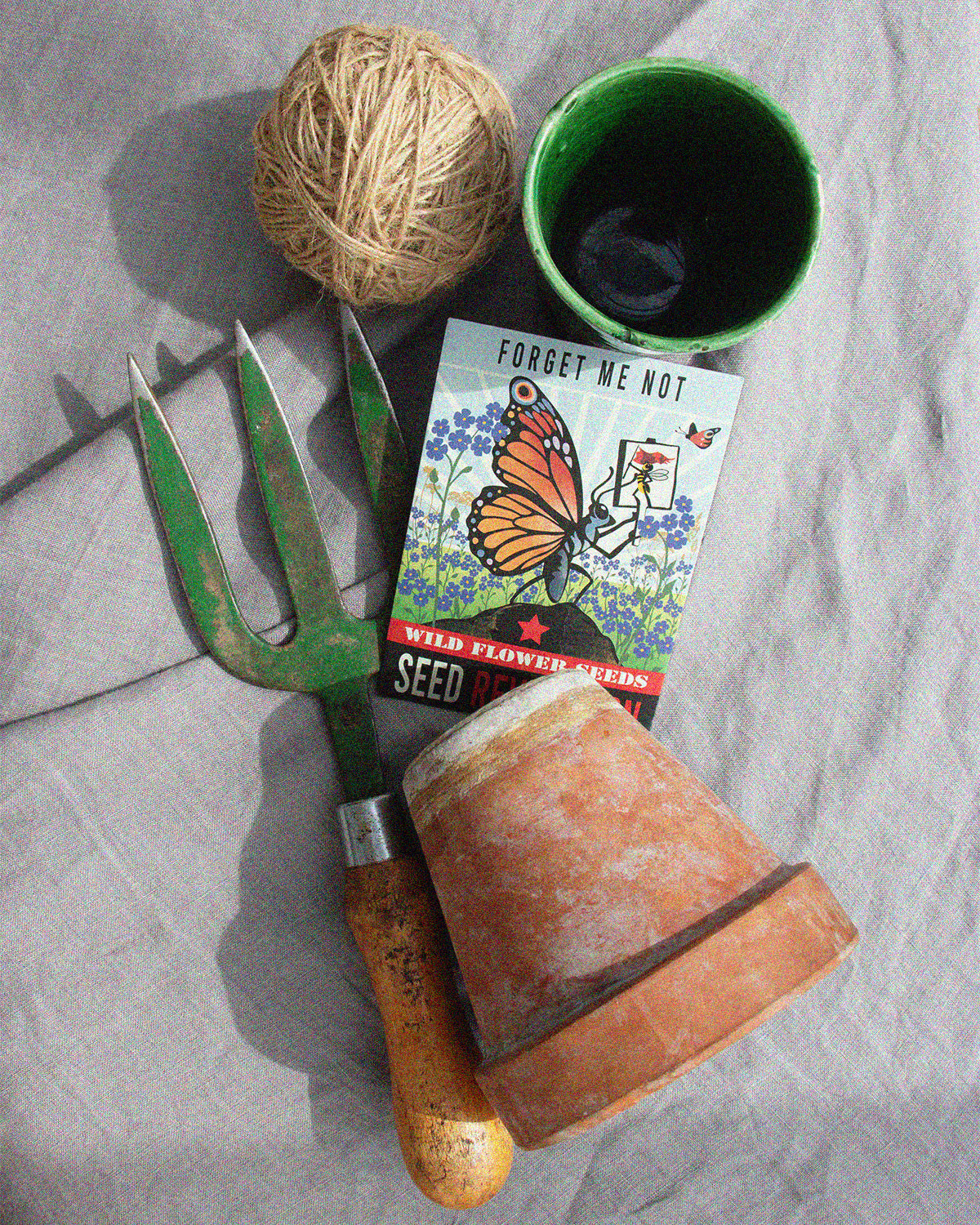Gardening tools, including a trowel and pots with forget me not wildflower seed packet, on a grey textured surface. Showcasing Seed Revolution's Forget Me Not, Myosotis Forget-Me-Not, Forgetmenot, flower forget me not, Myosotis flower, forget me not blooms, british wild flower seeds, british wildflower seeds, uk wildflower seeds.