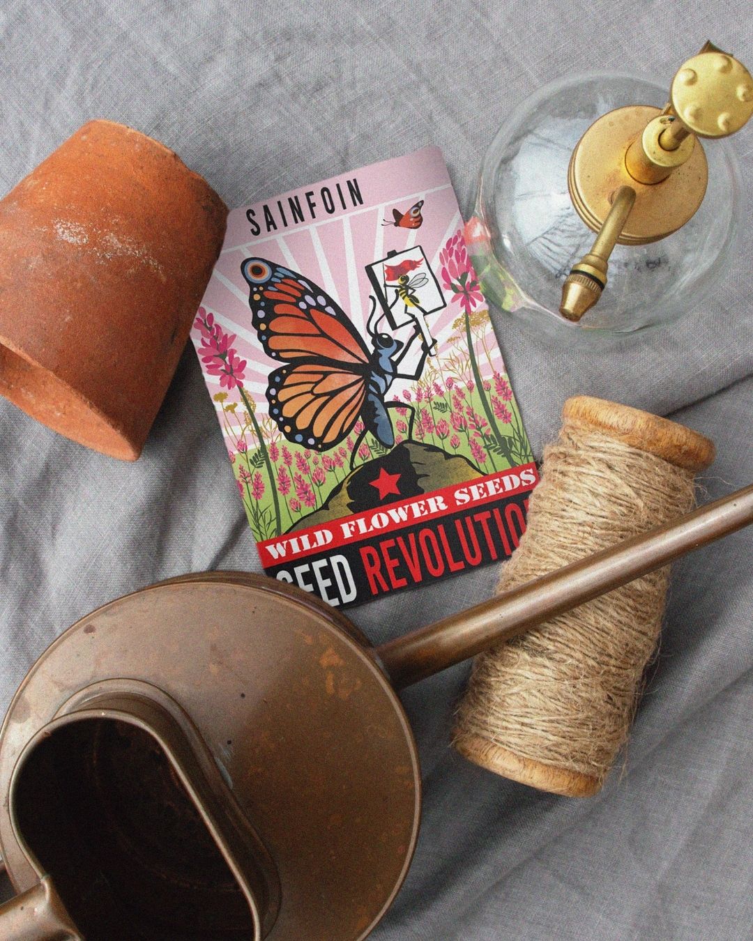Sainfoin wildflower seeds packet with gardening tools on a grey surface. Showcasing Seed Revolution's Onobrychis viciifolia, Sainfoin seed, Sainfoin seeds, Sainfoin Onobrychis viciifolia, british wild flower seeds, british wildflower seeds, uk wildflower seeds.