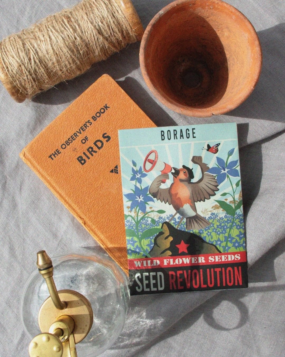 Wildflower borage seed packet with a bird illustration, next to gardening items. Showcasing Seed Revolution's Borago officinalis, borage seeds, borage flower, borage plant, british wild flower seeds, british wildflower seeds, uk wildflower seeds.