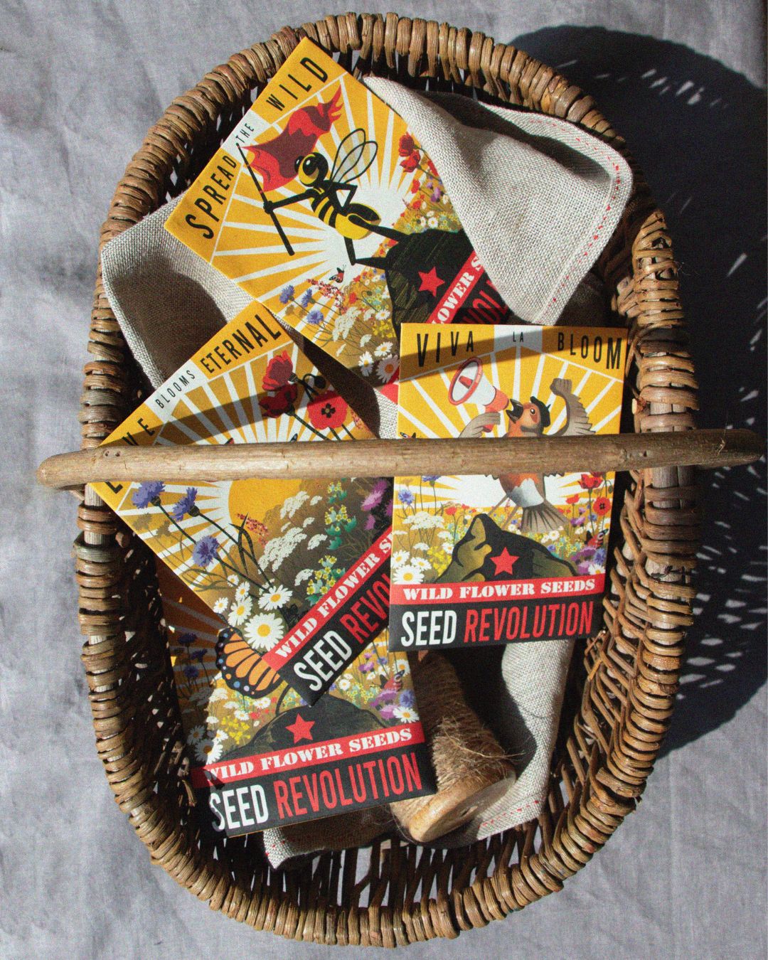 Wicker basket with colourful wildflower seed mix packets labeled on a grey textured surface. Showcasing Seed Revolution's british wild flower seeds, british wildflower seeds, wildflower mixes, mixed wildflower seeds, uk wildflower seeds, wildflower meadows, wildflower meadow, universal wildflowers, beginner meadow, cost-effective wildflower meadow, shade wildflowers, shady wildflower mix, wildflowers for pots, universal wildflowers.